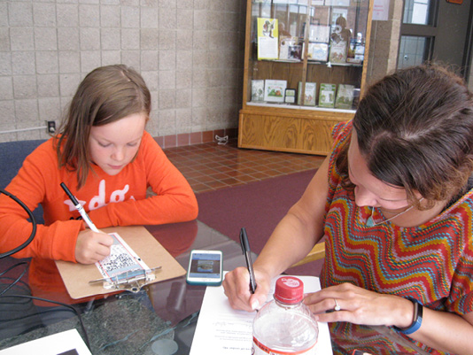 A woman and a girl writing at a desk.