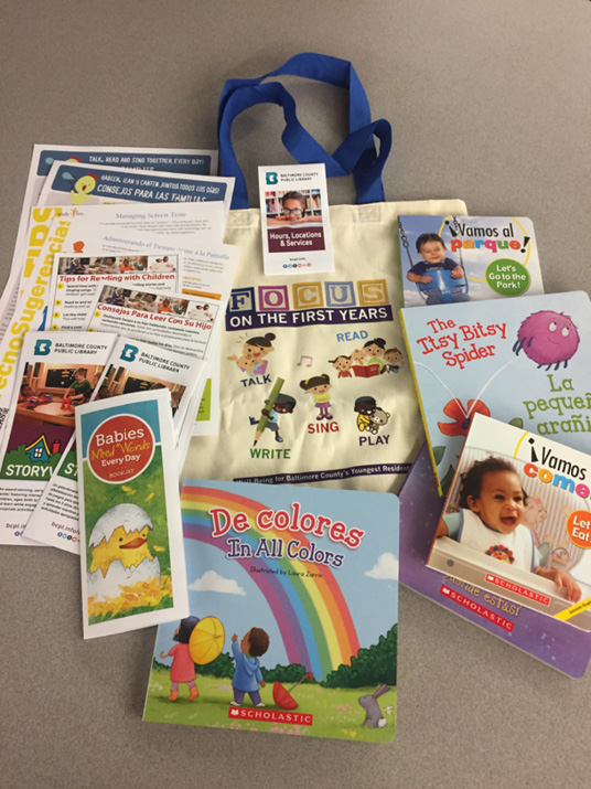 A bag with "FOCUS on the First Year" on the side, displayed with its contents: early literacy resources, including books, library card applications and fliers, information on early literacy programs and services, tip sheets for promoting the Every Child Ready to Read 2 practices, and Technology Tips for children ages birth to five