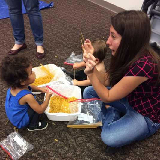 A librarian and small child play with dry noodles.