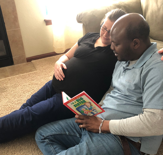 An expectant couple reads to their baby.