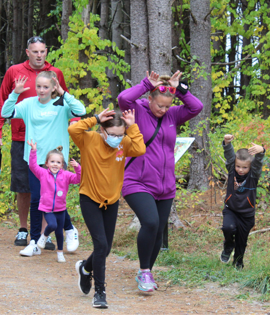 A Gorham family incorporates suggested movements while enjoying the StoryWalk; note this was photographed prior to the outdoor mask mandate in the area.