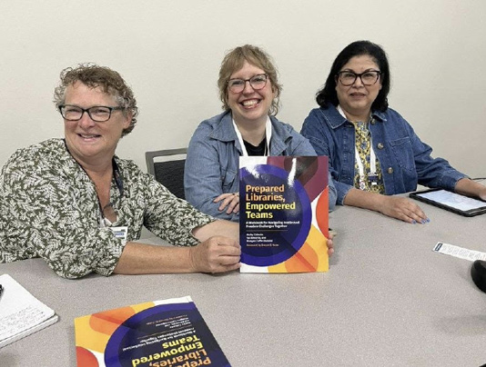 Val Edwards, Maegan Heindel, and Becky Calzada pose with copies of Prepared Libraries, Empowered Teams.